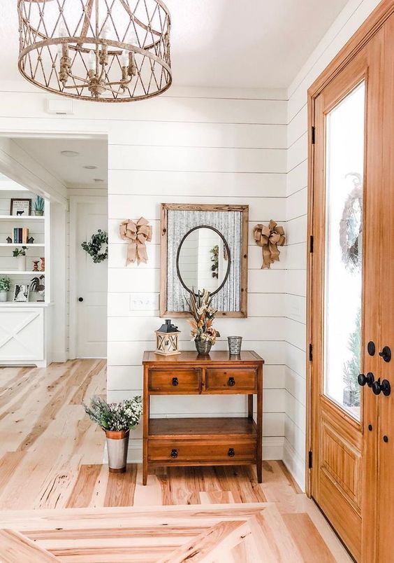 a cool modern farmhouse entryway featuring a stained console table, a mirror in a rustic frame, burlap bows and some floral arrangements