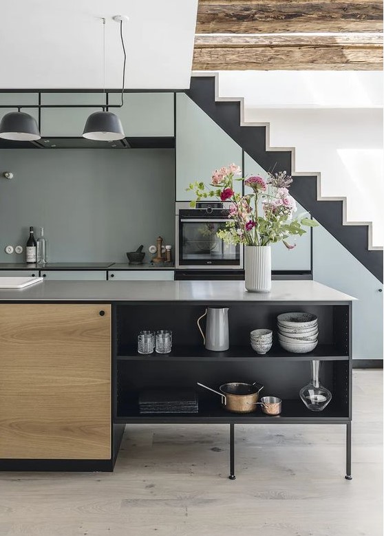 a cool modern kitchen with a staircase and pale blue cabinets built into it, a black and stained kitchen island