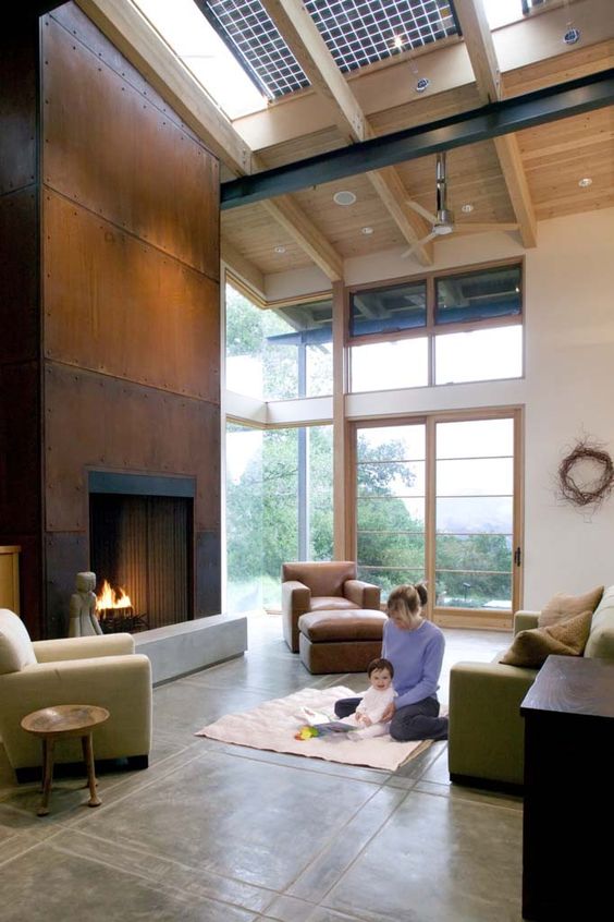 a double-height living room with a copper clad fireplace, green seating furniture, a tan chair and some lights