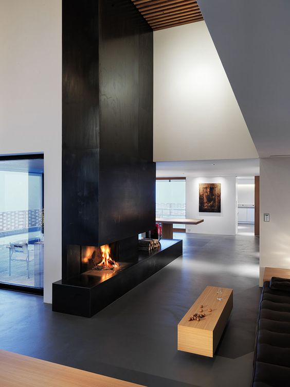 a minimal space with a black metal clad fireplace, a black sofa and a stained coffee table is amazing