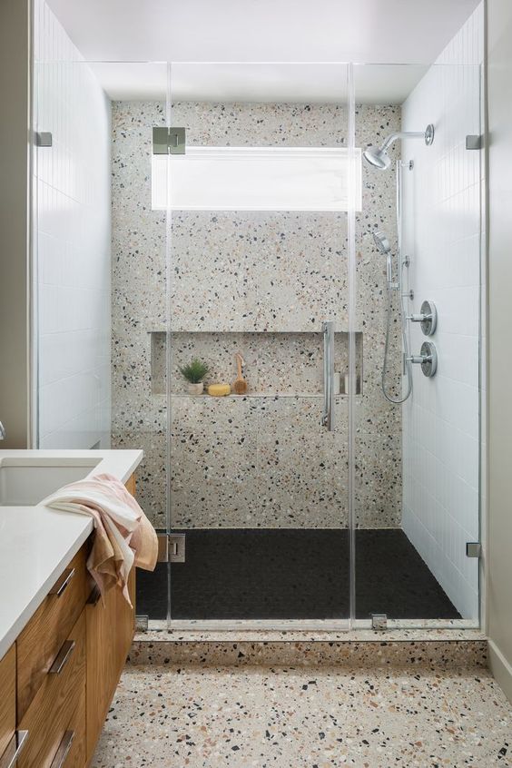a modern bathroom clad with neutral terrazzo, with a shower space, a stained vanity, a window in the shower for a fresher feel