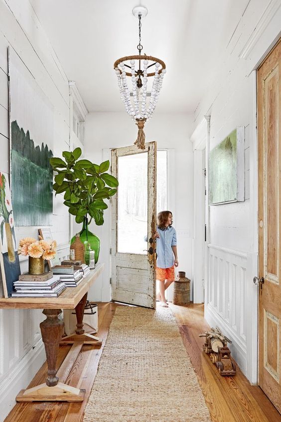 a modern farmhouse entry with a console table, some art, a bead chandelier, books and greenery is cool
