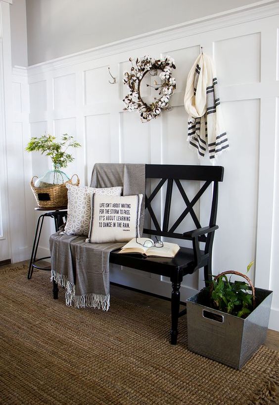 a modern farmhouse entryway with a black bench, a metal crate with greenery, a basket, a cotton wreath and some pillows
