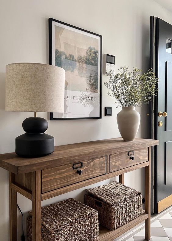 a modern farmhouse entryway with a stained console table, baskets, greenery in a vase, some art and a table lamp