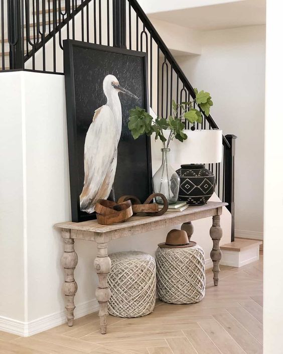 a modern farmhouse entryway with a whitewashed console table, woven poufs, some art and greenery is amazing