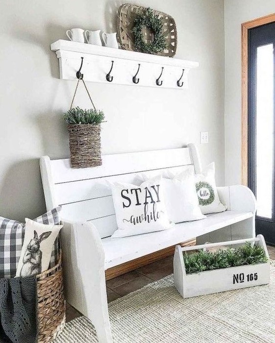 a modern farmhouse entryway with white furniture, a basket with pillows, a tool box and a basket with greenery