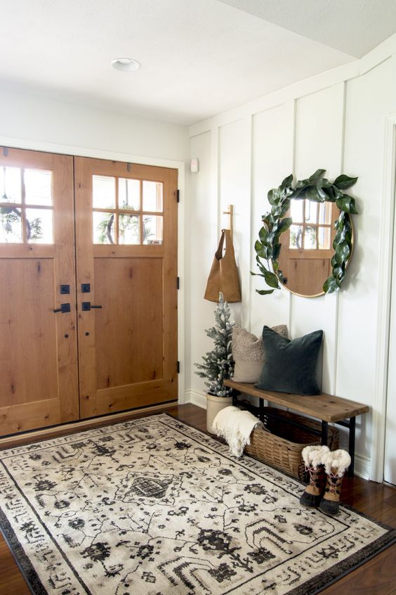 a modern farmhouse hallway with a wooden bench, a basket for storage, a mirror covered with greenery and a large boho rug