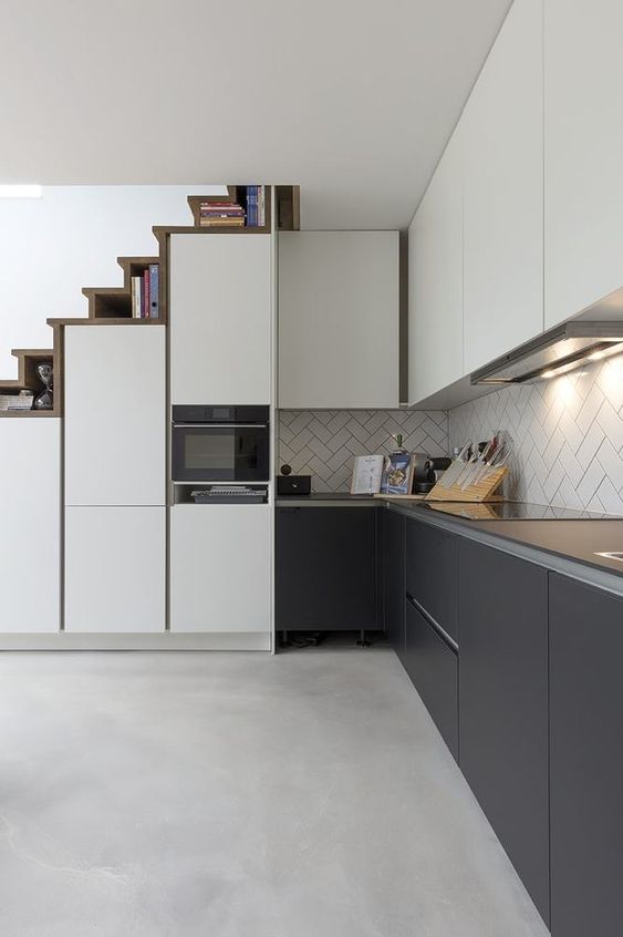 a modern graphite grey and white kitchen with slek cabinets, a herringbone tile backsplash and built-in lights