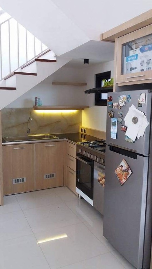 a modern kitchen with lower timber cabinets placed under the stairs, with open shelves with lights and a couple of appliances