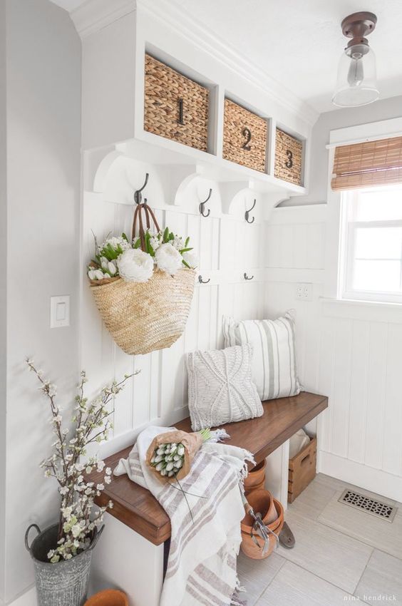a neutral modern farmhouse mudroom with a built-in bench and baskets, lots of blooms and greeneyr, some pillows
