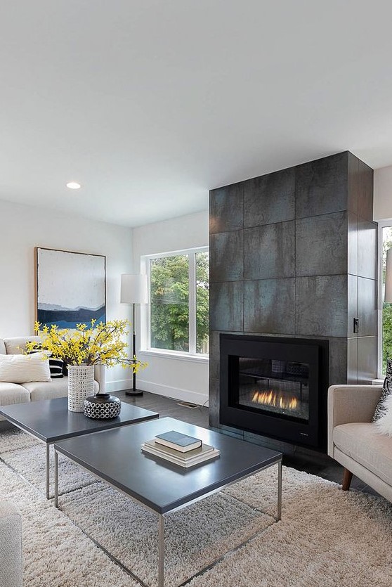 a neutral modern living room with two dark coffee tables and a large fireplace clad with aged metal sheets