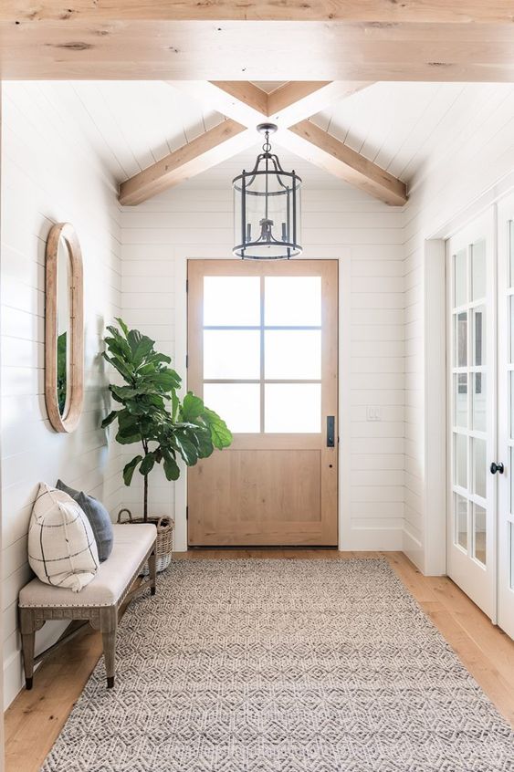 a simple modern farmhouse entry with shiplap walls, an upholstered bench, a tree in a basket, a mirror and a pendant lamp