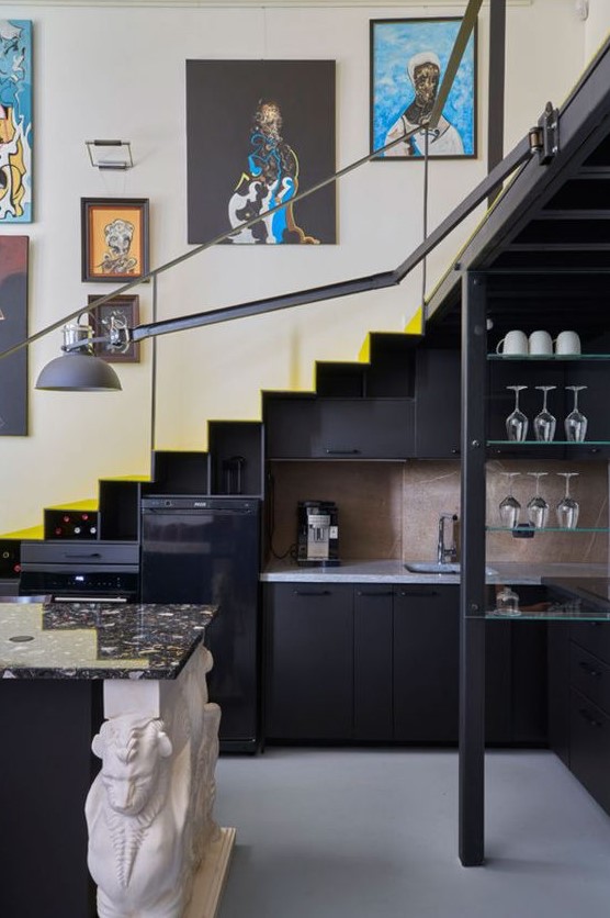 a staircase with a built-in black kitchen, open glass shelves, a kitchen island, some decor and a black sconce