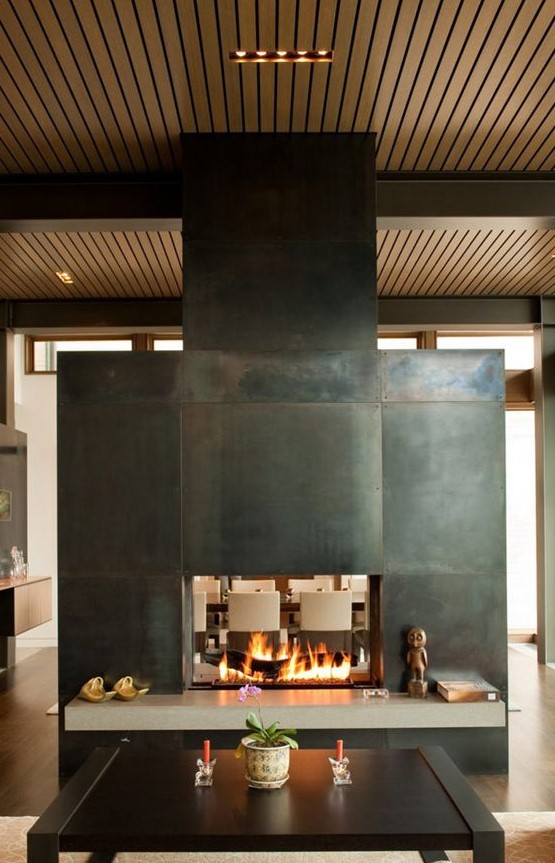 a stunning two-sided fireplace clad with metal sheets to separate the living and dining room and give coziness to both
