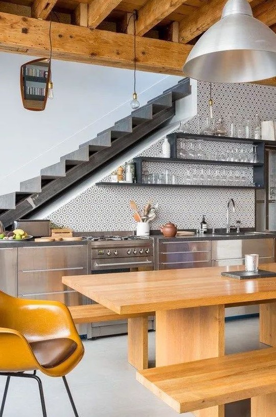 a stylish modern kitchen placed at the staircase, with metal cabinets, open shelves, a timber dining set and pendant lamps