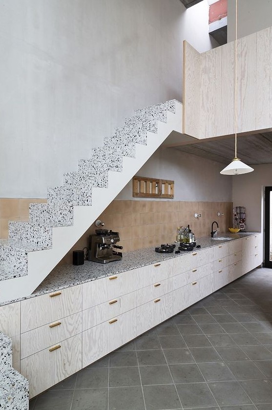 a stylish modern kitchen with whitewashed lower cabinets under the stairs, a tile backsplash and terrazzo countertops
