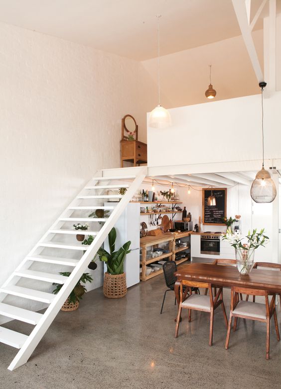 a stylish modern loft with a kithen squeezed under the stairs, open storage units and potted greenery, a dining space next to it