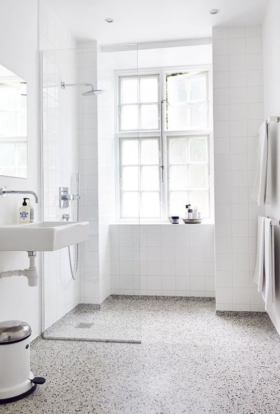 a white airy bathroom is accented with a terrazzo floor of grey, white and black and clad with white square tiles