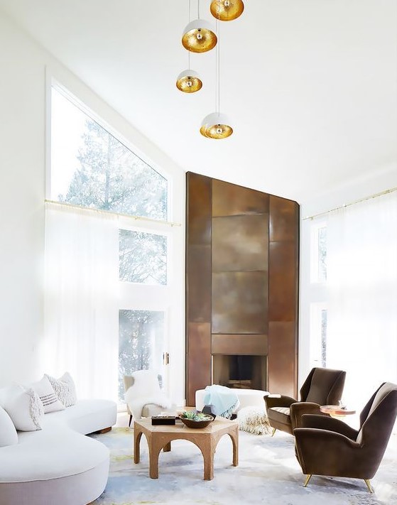 a white living room with an attic ceiling, brown chairs with gold legs and a fireplace clad with copper sheets that bring color in