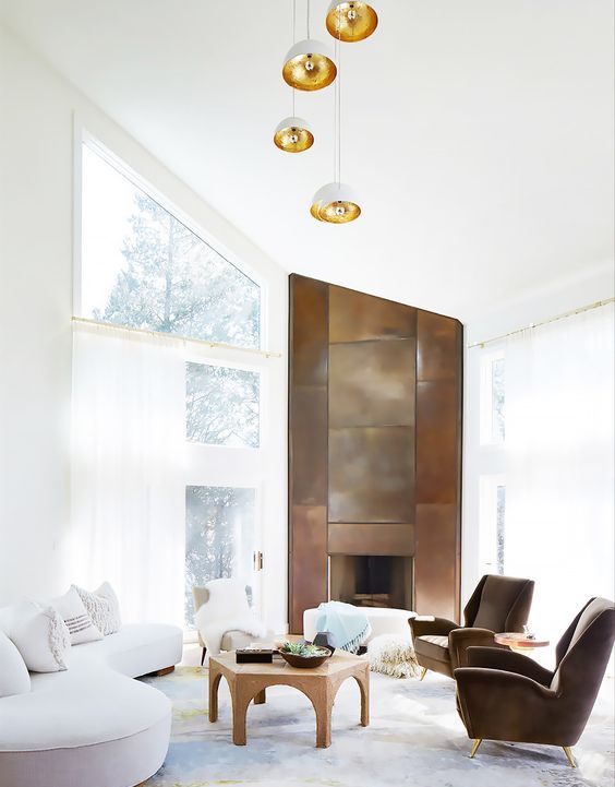 an airy living room with a copper clad firepalce, a white curved sofa, a coffee table and taupe chairs