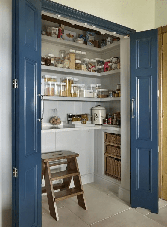 A small and chic pantry with built-in cupboards, open shelves, baskets, a wooden stool and some glasses is a super cool idea
