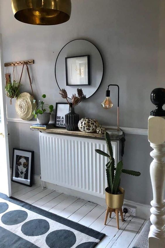 A Scandinavian boho room with a small radiator covered with a shelf with decor and a lamp, a mirror and some plants