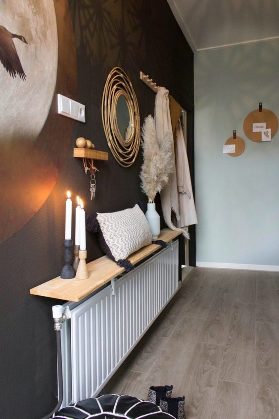 a long radiator with a long and narrow shelf that serves as decoration, candles, a pillow and pampas grass