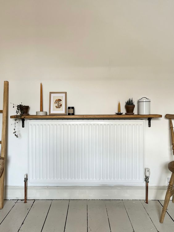 A minimal room with a long and narrow radiator and a stained shelf with candles and decor is cool