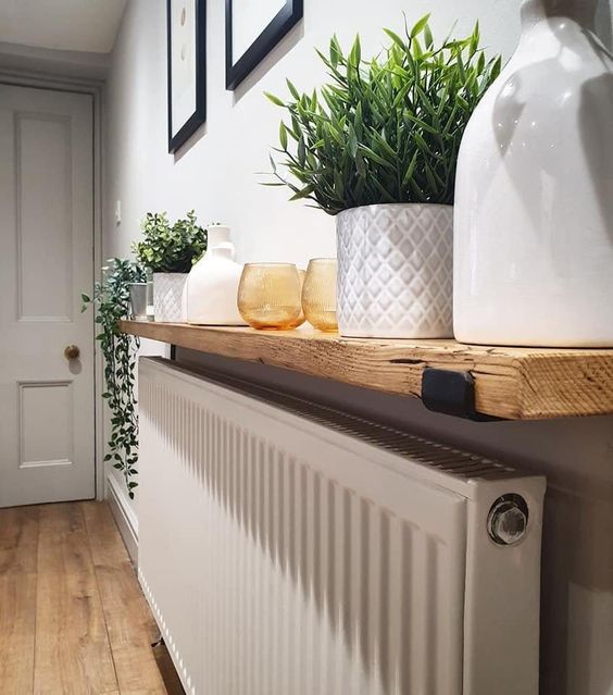 a radiator hidden with a light stained shelf used to store and display the plants