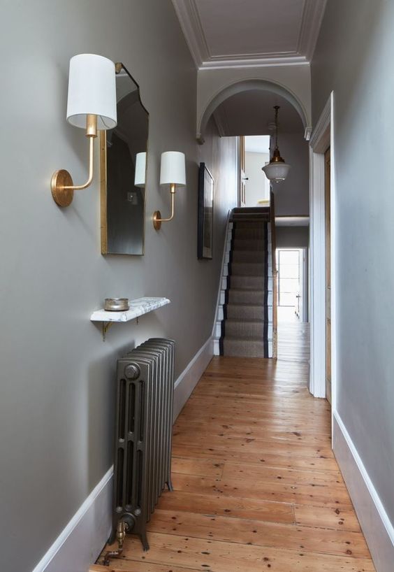 a small and elegant entrance area with a dark radiator and a small shelf above it, with a mirror and sconces