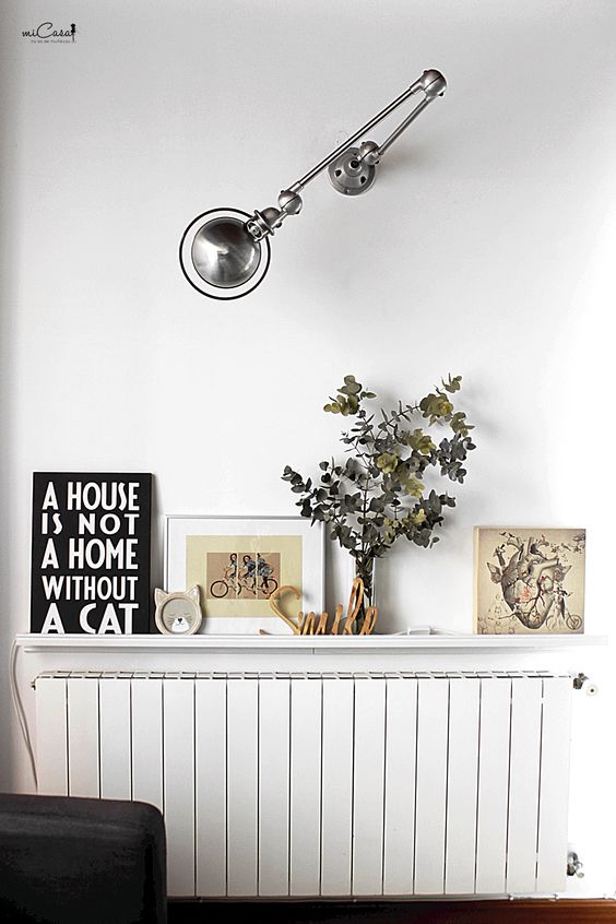 A white radiator with a matching white shelf and cool decor on it, with a wall lamp giving the radiator a unified look