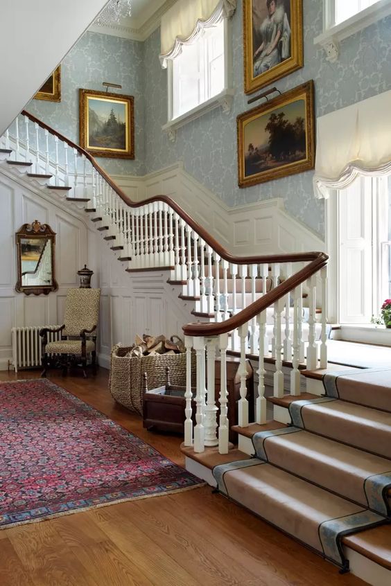 A historic home with light stained floors, dark stained railings, white paneling and lots of sophisticated vintage artwork