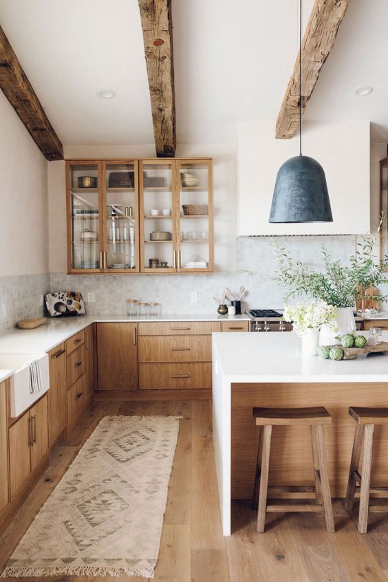 a beautiful and tranquil kitchen with reclaimed wood beams, light stained cabinets, white stone countertops and a black pendant lamp