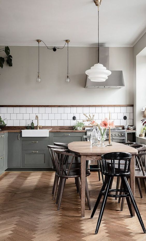 a modern Scandi kitchen with a white tile backsplash, dark stained countertops, a herringbone wood floor, a light stained table, dark stained chairs and a black chair