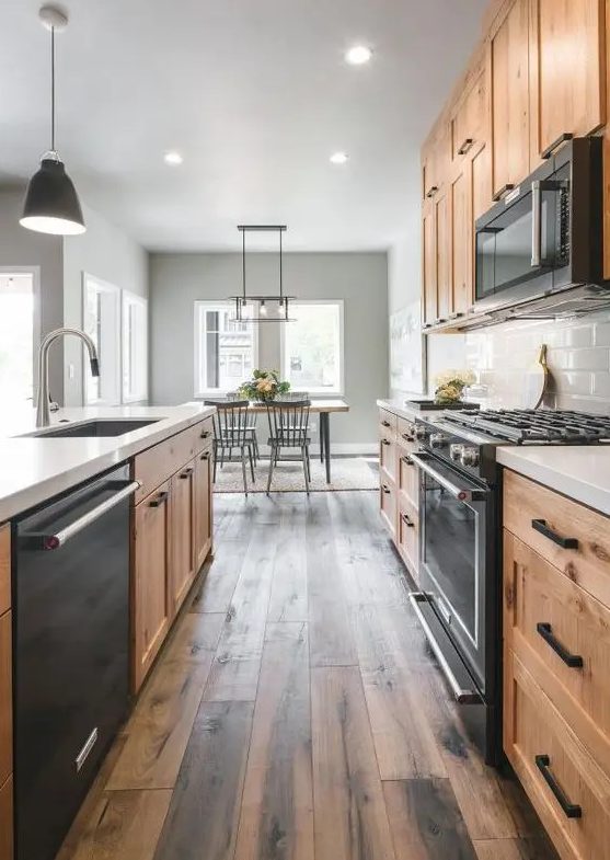 A modern farmhouse kitchen with light stained cabinets, black appliances, and a dark reclaimed wood floor is amazing