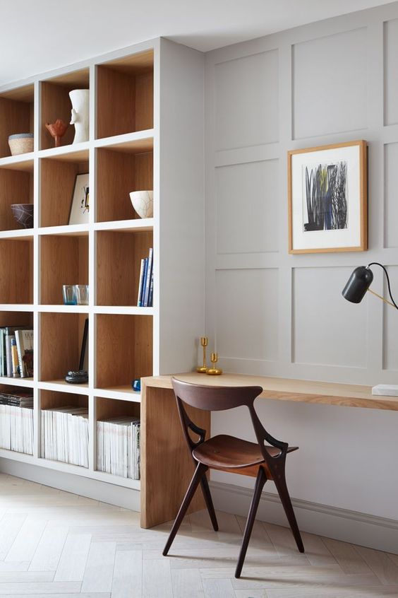 A modern dove gray home office with a large shelf, a stained desk, a dark stained chair and a blonde wood picture frame