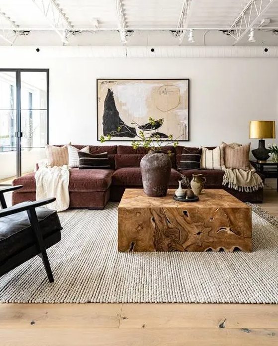 an elegant living room with a burgundy sitting area, a black chair, a light stained wood floor, a neutral rug and a richly stained wood table