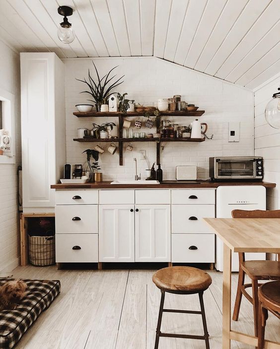 a white Scandi kitchen with sleek cabinets, a light wood table and matching chairs, and dark-stained butcher block countertops