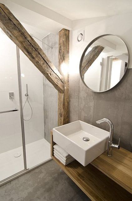 a modern concrete-clad bathroom with a wooden column and beam, a floating vanity, a round mirror and a sink