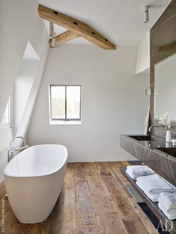 a modern white bathroom with weathered wood floors, a wooden beam, a floating black marble vanity and a large mirror