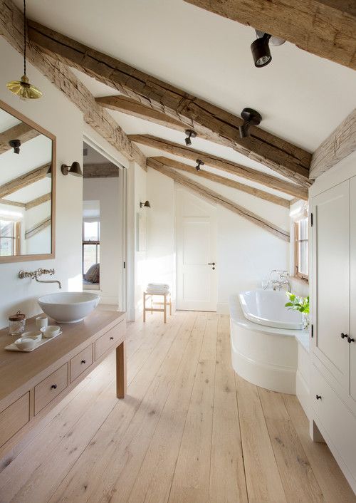 a neutral bathroom with exposed beams and hardwood floors, a light-stained vanity, a paneled bathtub, and a large closet and large mirror