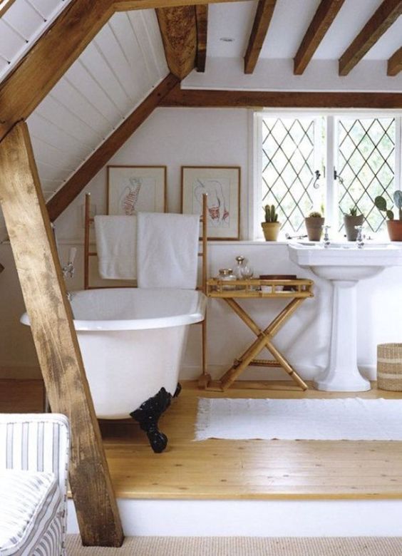 a rustic bathroom with a platform clawfoot tub, freestanding sink, wooden beams, potted plants and some artwork