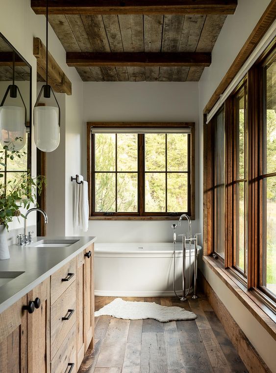 a rustic bathroom with wooden floors, a beamed ceiling, a wooden vanity, a hanging lamp, some windows and a vintage bathtub