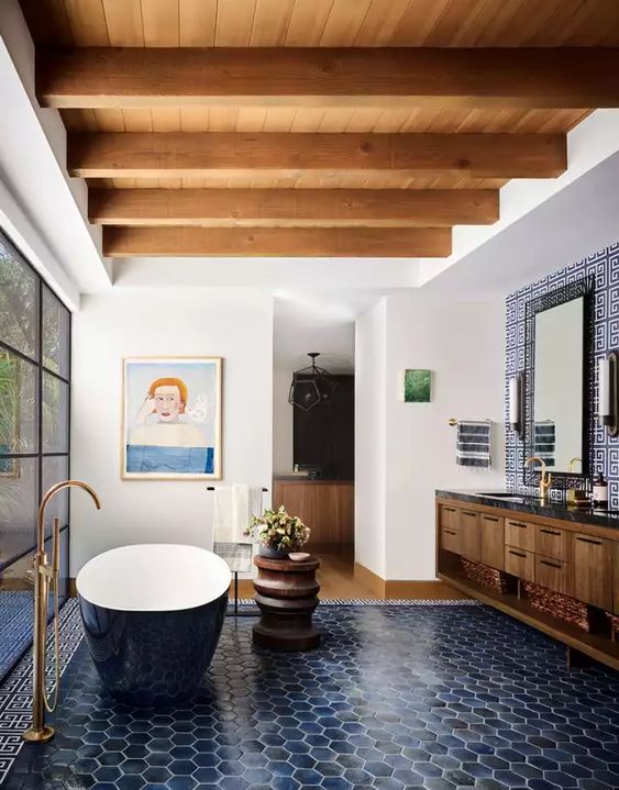 a stylish bathroom with wooden beams, navy hexagonal tiles, a navy oval bathtub, a floating vanity and some art, as well as a glass-enclosed shower area