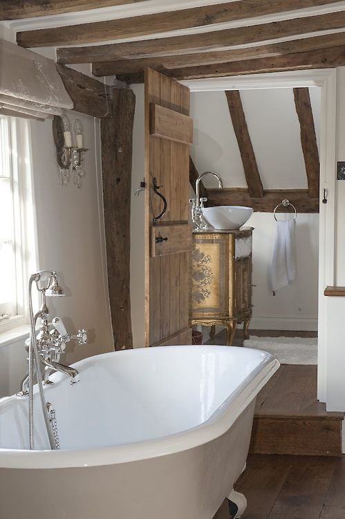 a vintage bathroom with wooden beams and floors, a separate room with a vintage vanity and a claw-foot bathtub