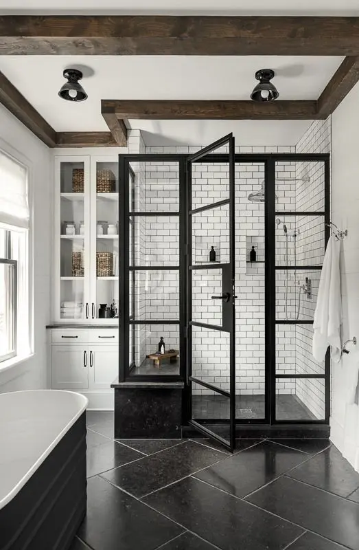 a black and white farmhouse bathroom with subway tiles and black flooring, a shower area, built-in storage and a black soaking tub
