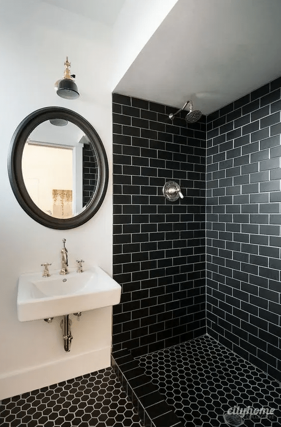 a striking bathroom with black subway tiles in the shower, black hexagon tiles on the floor, a mirror in a black frame and a wall-mounted sink