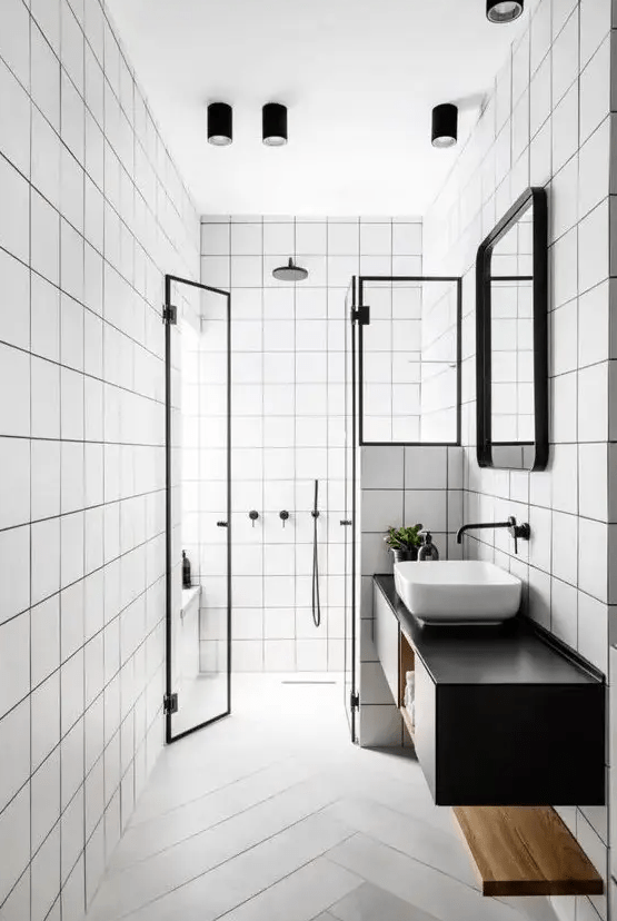 a modern bathroom with white square tiles, a floating black vanity, a shower area, a sink, a mirror in a frame and some lights