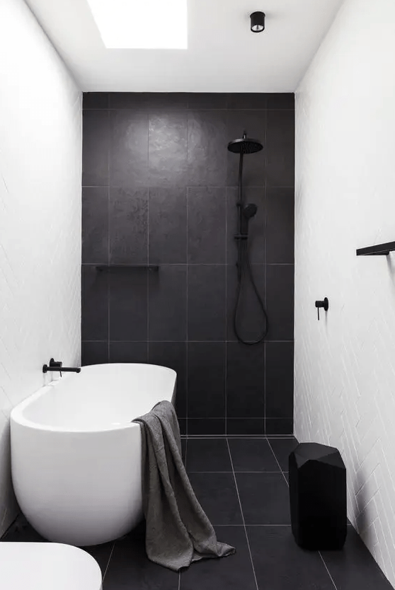a contrasting herringbone bathroom with large format tiles, an oval bath, a black stool and black fittings