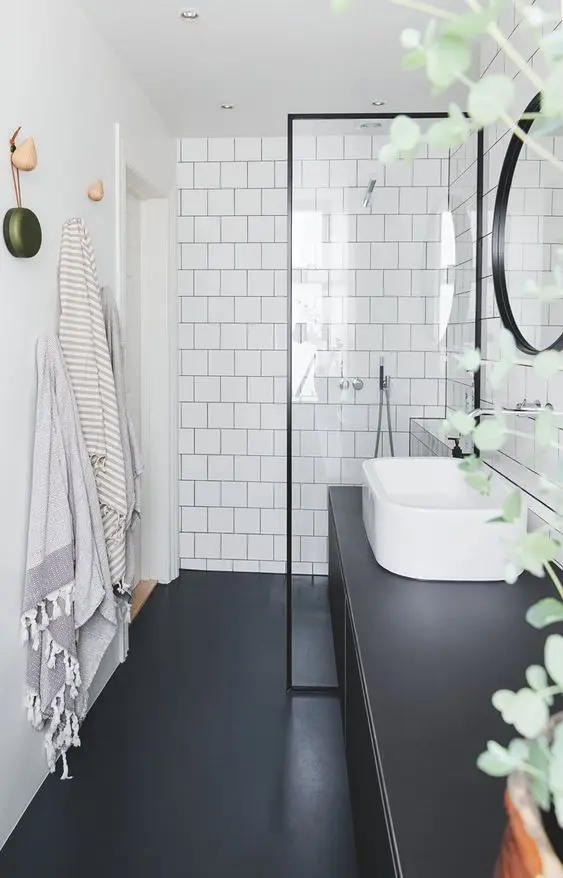 a black and white bathroom with square tiles, a black floor and a large black vanity and a round mirror in a black frame